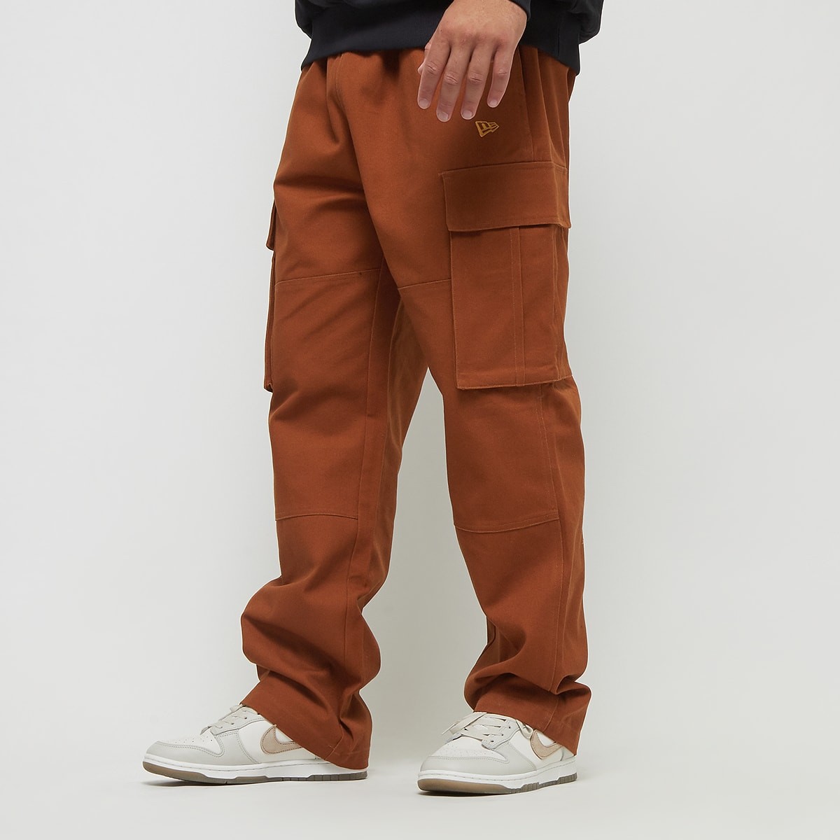 Brown cargo trousers featuring multiple pockets, a relaxed fit, and a subtle New Era logo, paired with white sneakers for a casual look.