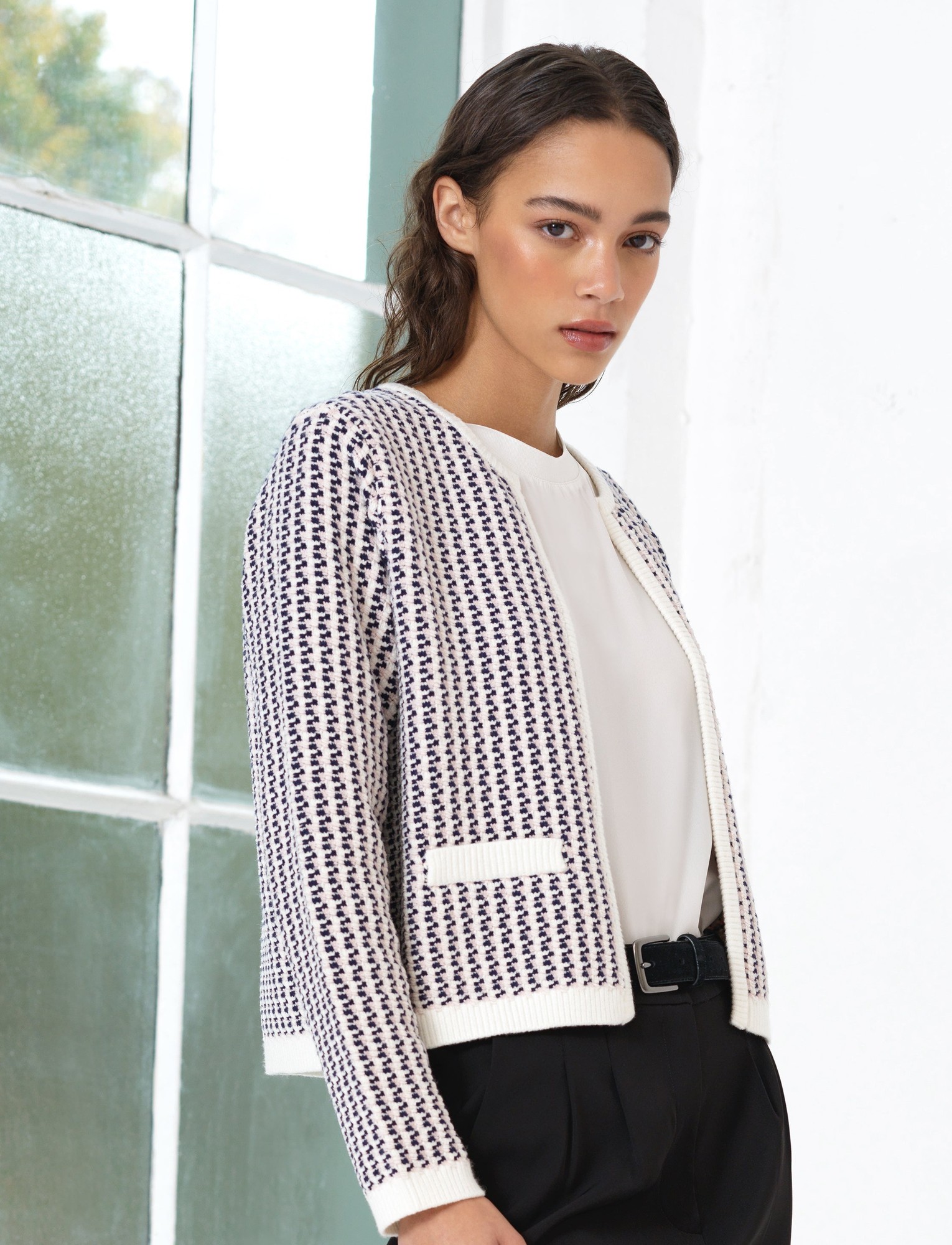 Textured knit cardigan in navy and cream with a fitted silhouette, round neckline, and front pockets, styled with a light blouse and black trousers.