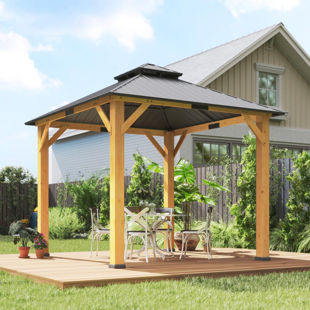 Grey double-tier hardtop gazebo with a wooden frame, featuring a sloped roof and open sides, set on a wooden deck with a table and chairs surrounded by greenery.