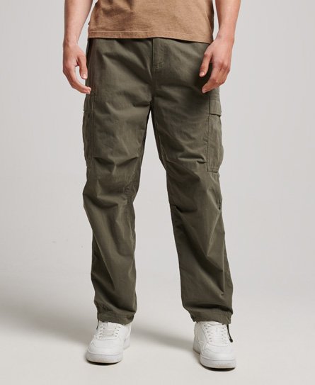 Olive green parachute trousers by Superdry, featuring a relaxed fit, multiple cargo pockets, and adjustable cuffs, paired with white sneakers.