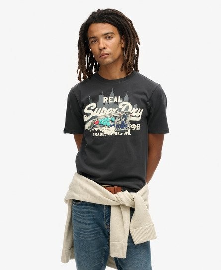 Black patterned T-shirt featuring a colorful "Superdry" graphic with a New York theme, made of soft cotton, paired with light blue jeans and a cream sweater tied around the waist.