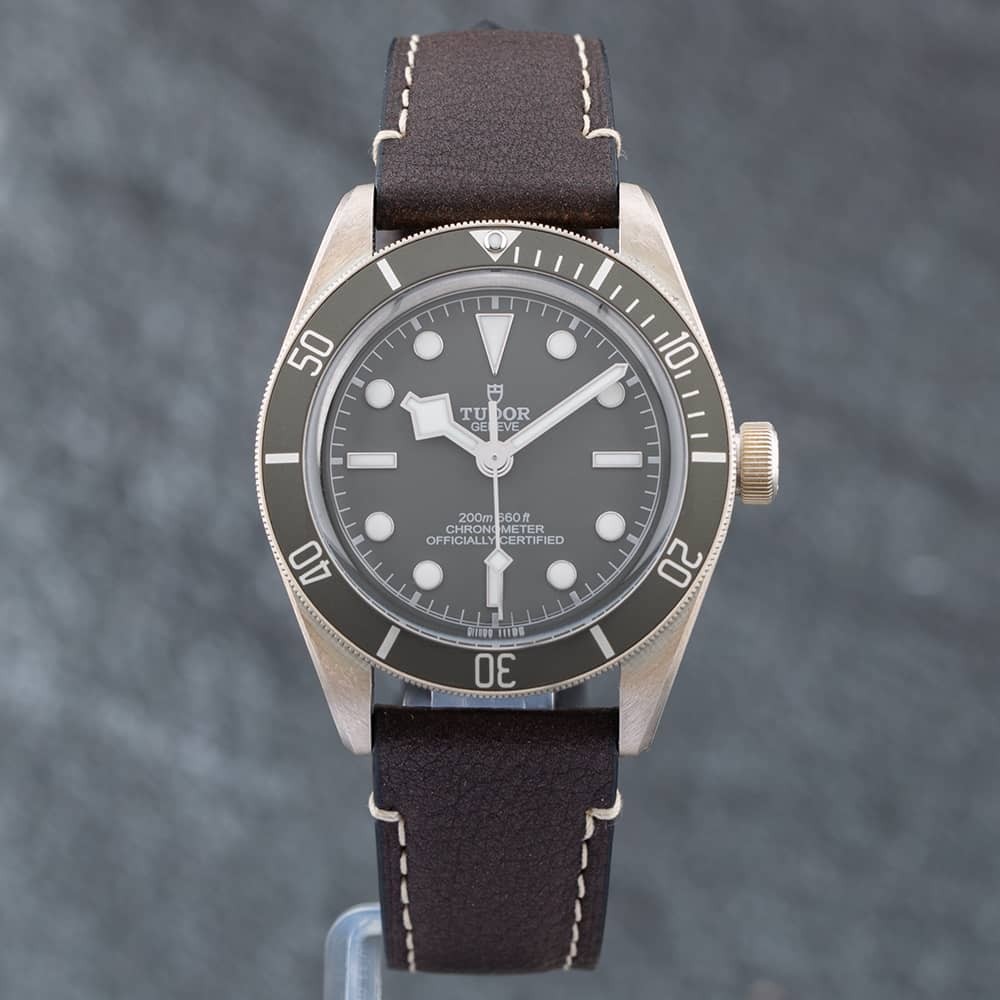 Tudor Black Bay 58 watch featuring a stainless steel case, black bezel, grey dial with luminous markers, and a brown leather strap with white stitching.