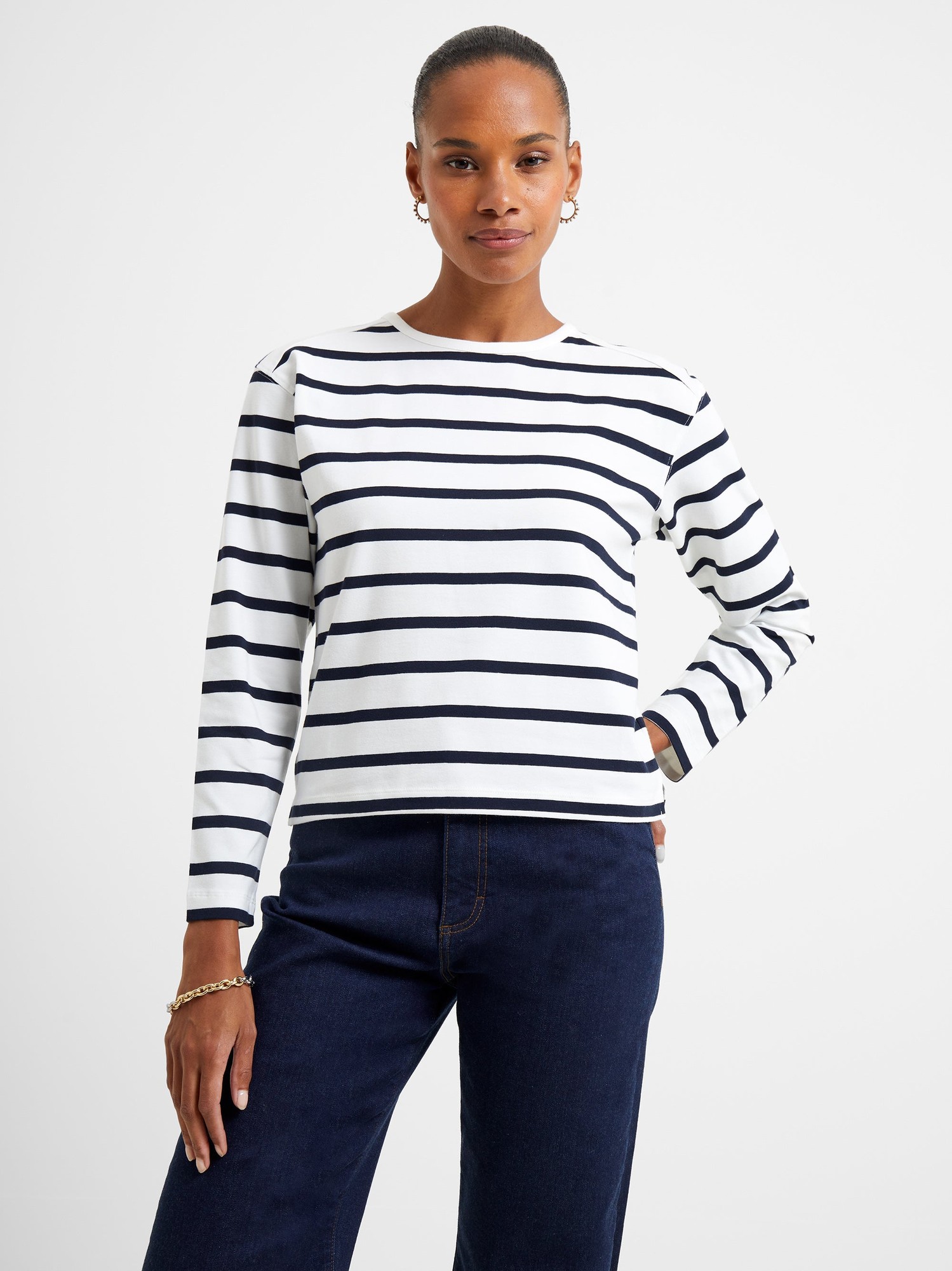 White long-sleeve top with navy horizontal stripes, featuring a slash neck design and relaxed fit, paired with dark denim jeans.