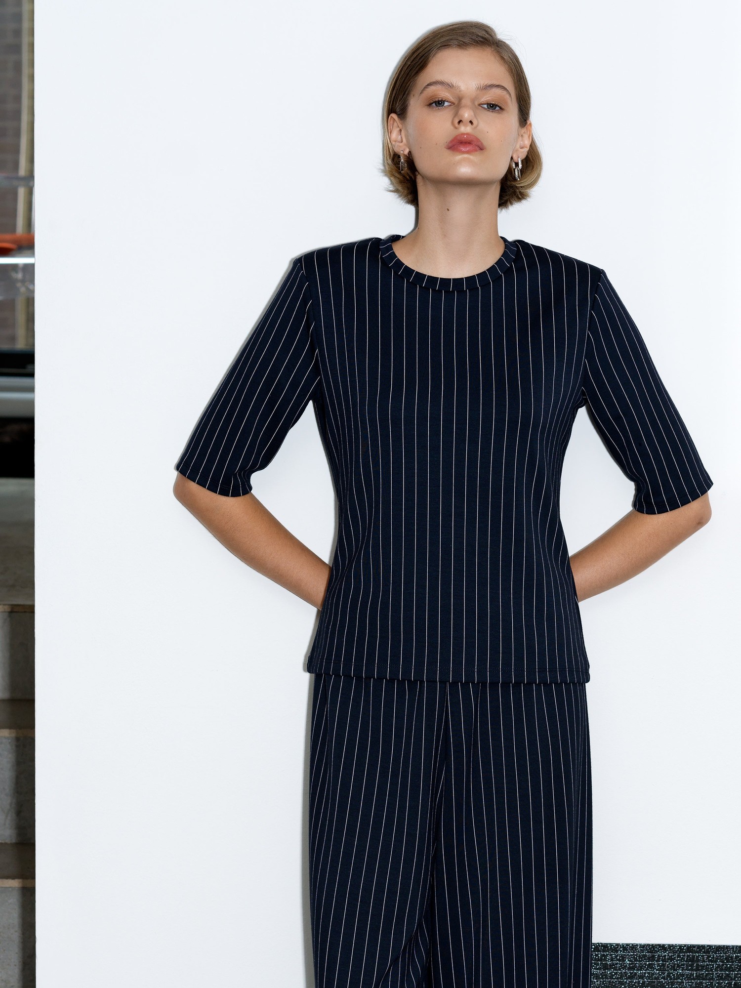 Navy blue jersey T-shirt with white pinstripes, featuring shoulder pads and short sleeves, styled with a round neckline and a fitted silhouette.