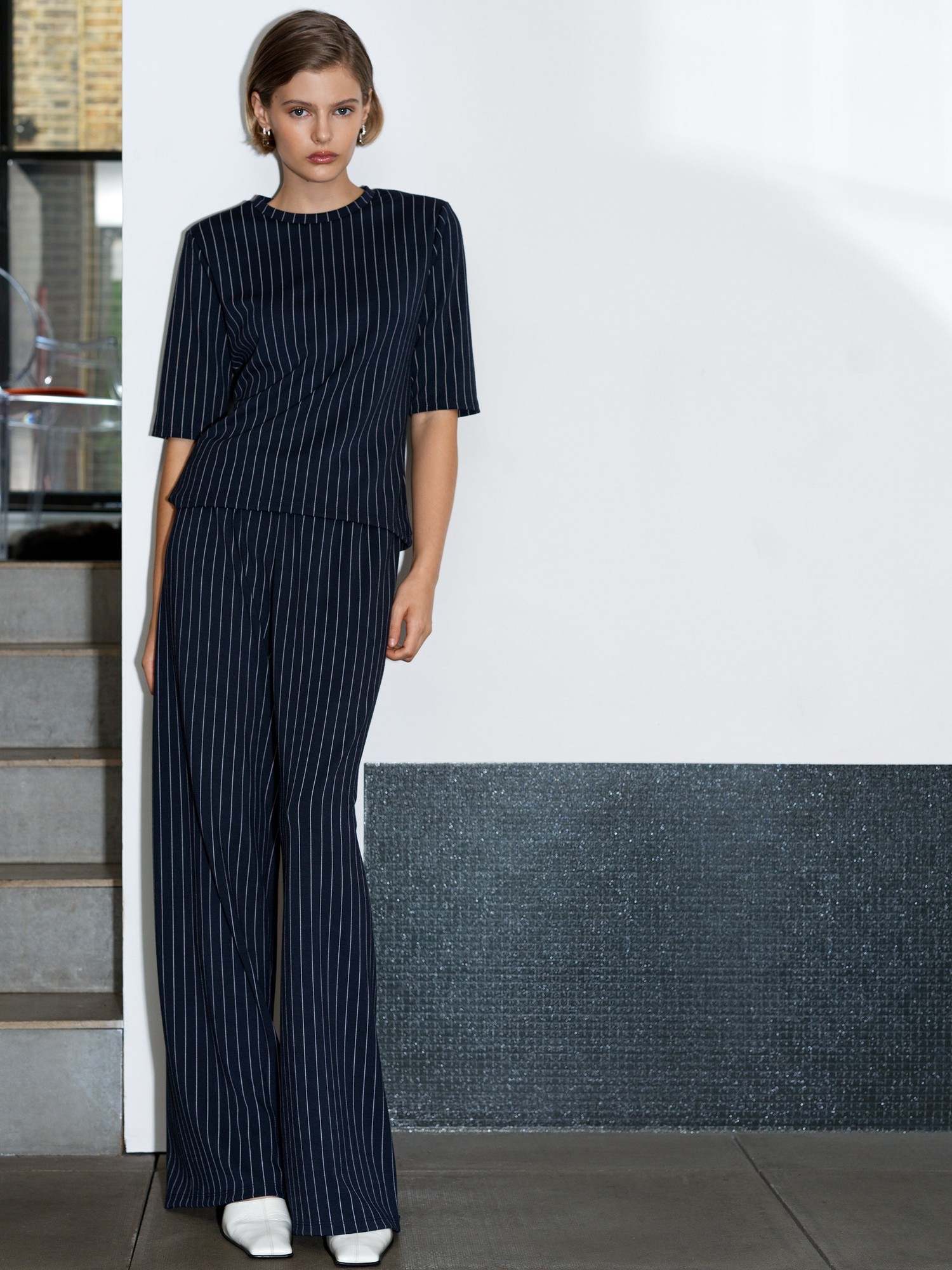 Navy and white pinstripe wide-leg trousers made of jersey fabric, featuring a high waist and a relaxed fit, styled with a matching top for a coordinated look.