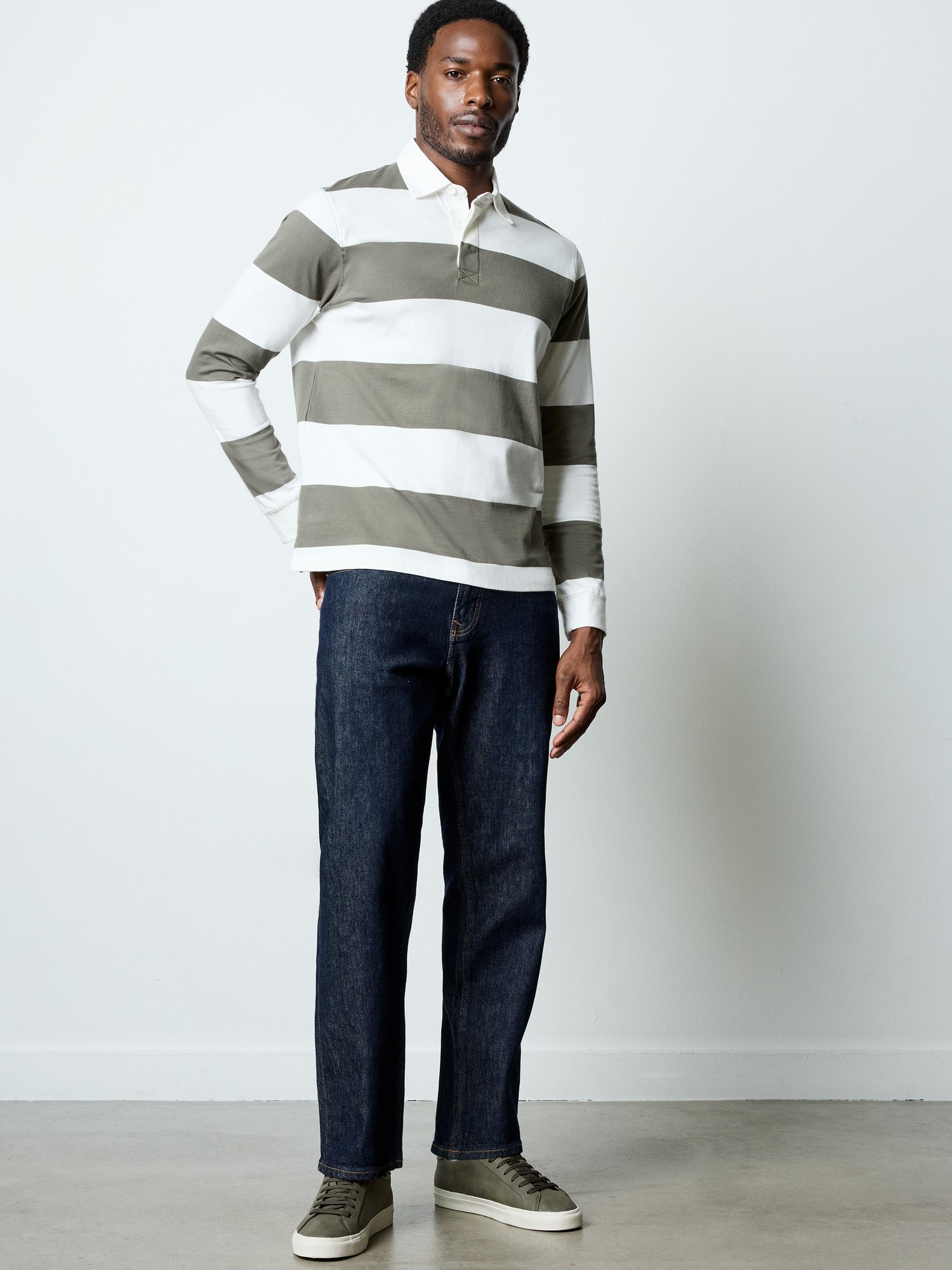 Relaxed fit deep blue selvedge jeans with a classic five-pocket design, paired with a striped long-sleeve polo shirt and casual sneakers.