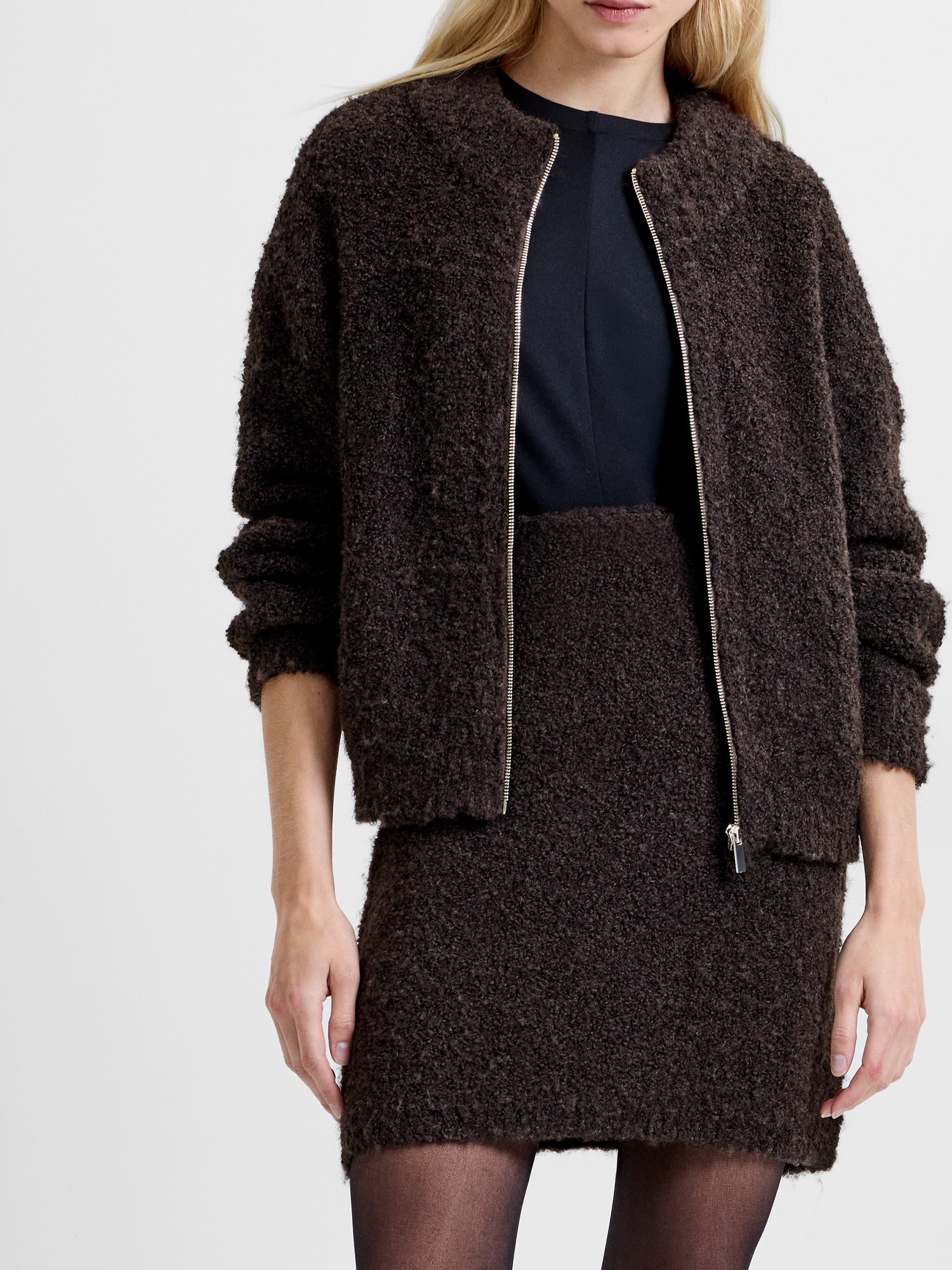 High-waisted mini skirt in rich brown boucle fabric, featuring a textured finish, paired with a matching cropped jacket and worn with black tights.