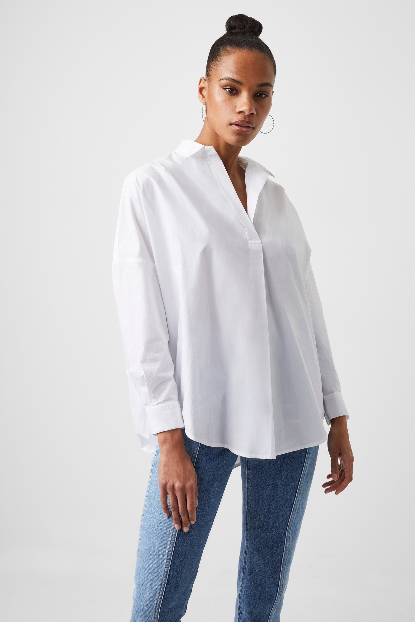 White poplin popover shirt with a relaxed fit, featuring a collar, long sleeves, and a buttonless placket, paired with light blue jeans.