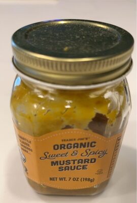 Glass jar with a gold metal lid, filled with yellow mustard sauce; label features orange and black text stating "Organic Sweet & Spicy Mustard Sauce," net weight 7 oz.