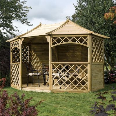 Wooden gazebo with a natural finish, featuring a peaked roof, lattice side panels, and an open interior with seating and a table, set in a grassy outdoor area.