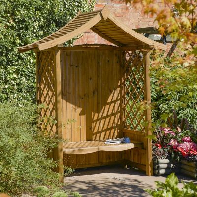 Wooden arbour featuring a slatted roof, lattice side panels, and a curved bench, set against a backdrop of greenery and colorful flowers.