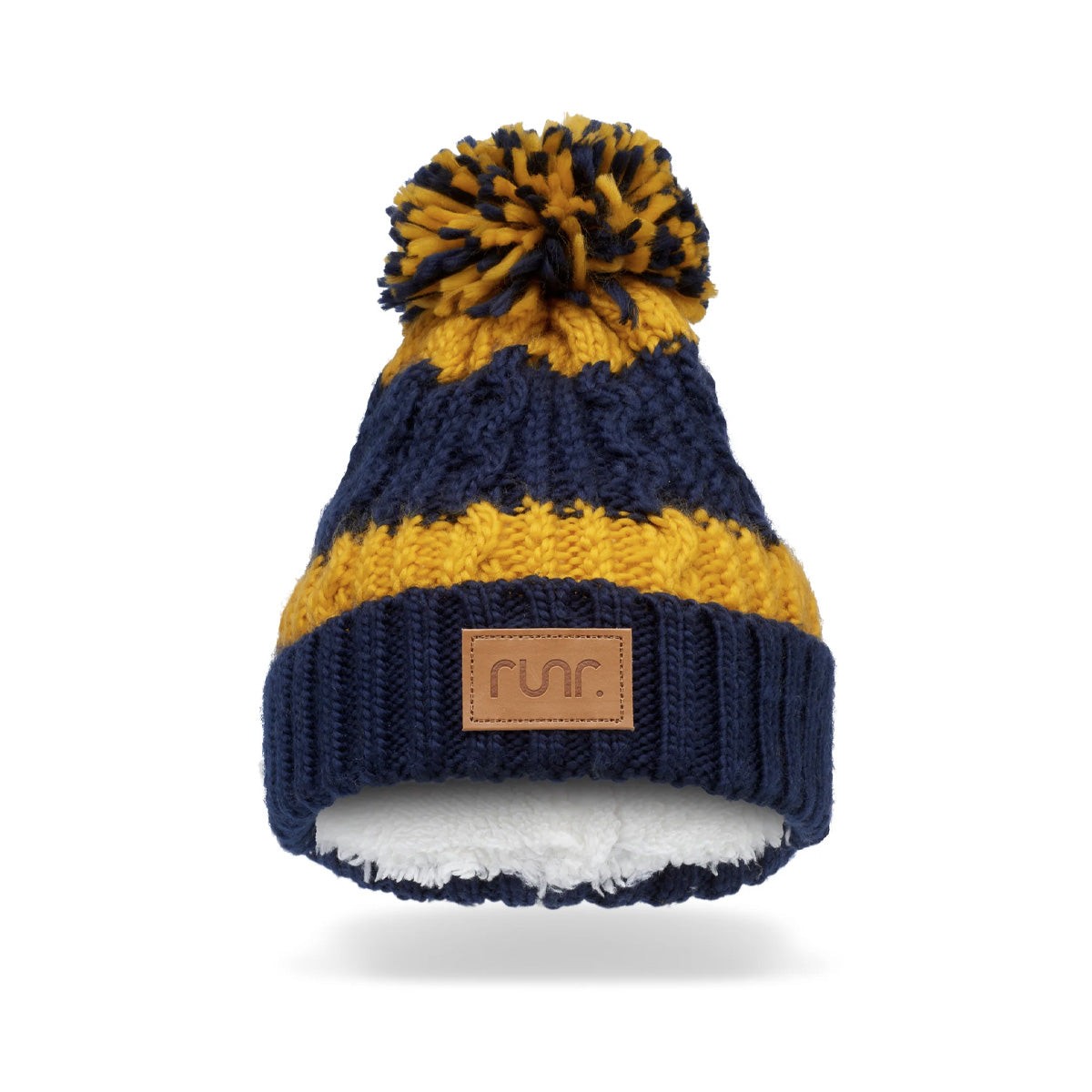 Navy blue and mustard yellow knitted bobble hat with a large pom-pom on top, featuring a soft, white fleece lining and a brown leather Runr logo patch on the front.