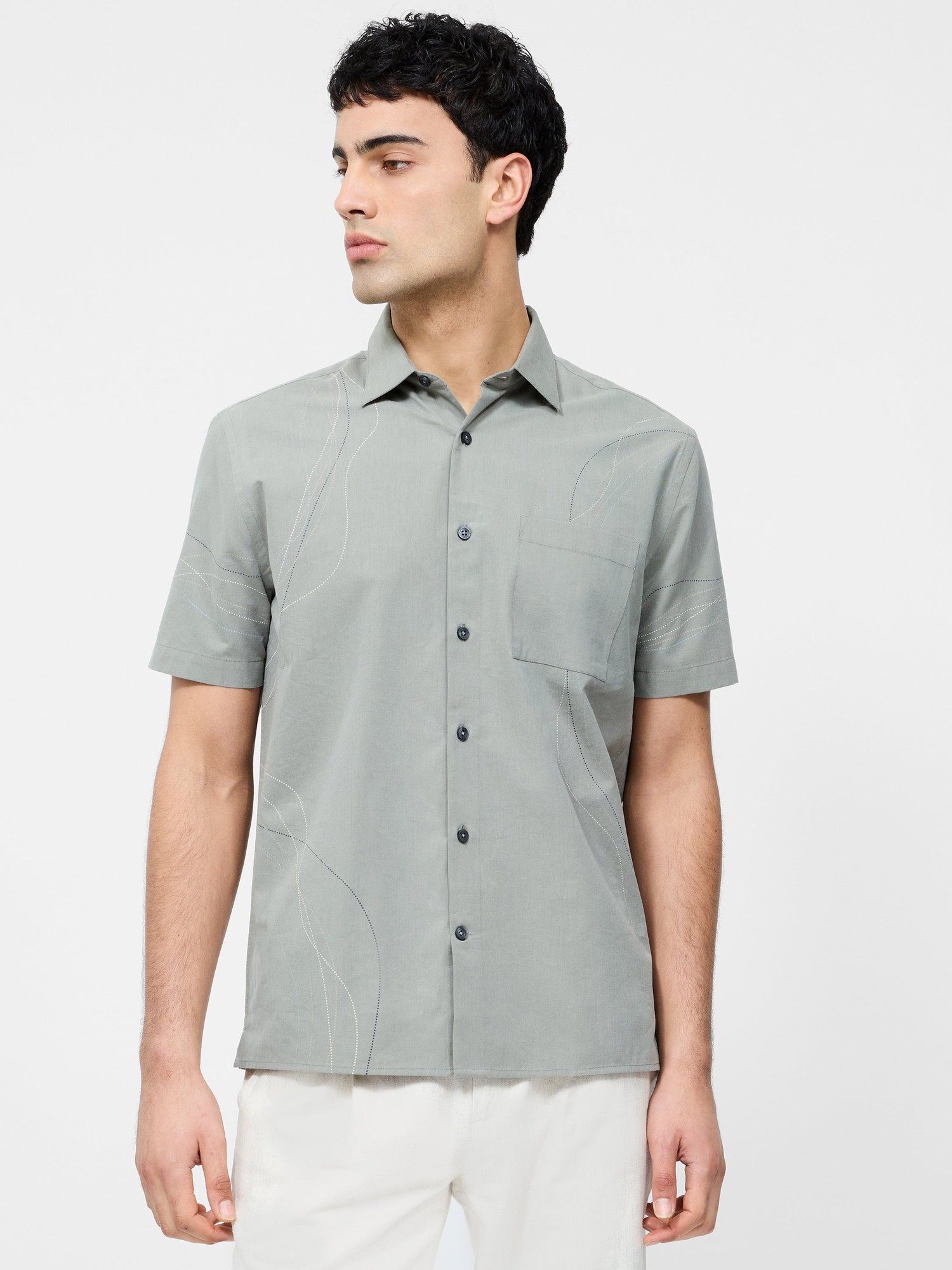 Sage green short sleeve shirt featuring a subtle scribble dot pattern, a chest pocket, and a button-up front, made from lightweight fabric.
