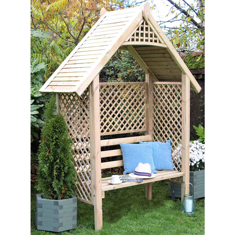 Wooden garden seat in natural finish with a decorative trellis back, slanted roof, and two planters on either side, featuring cushions and a small table.