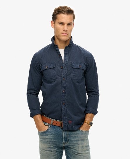 Navy long sleeve military shirt by Superdry featuring a button-up front, two chest pockets, and a classic collar, paired with light blue jeans and a brown belt.