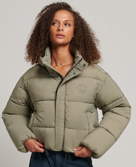 Short puffer jacket in olive green with a cropped silhouette, featuring a high collar, zip closure, and Superdry logo on the chest, made from a soft, quilted material.