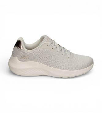 Beige slip-on Skechers sneakers with a textured upper, round toe, and a cushioned sole, featuring subtle metallic accents on the heel.