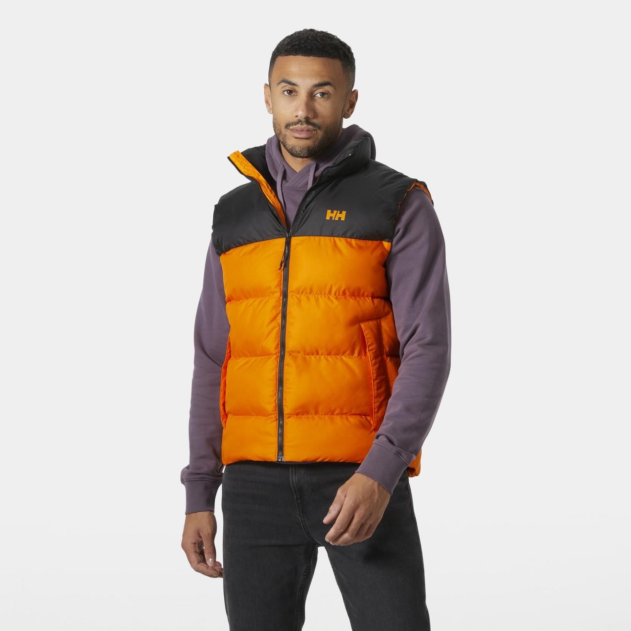 Sleeveless down jacket in vibrant orange with a black upper, featuring a zip front, high collar, and Helly Hansen logo on the chest, paired with a purple hoodie underneath.