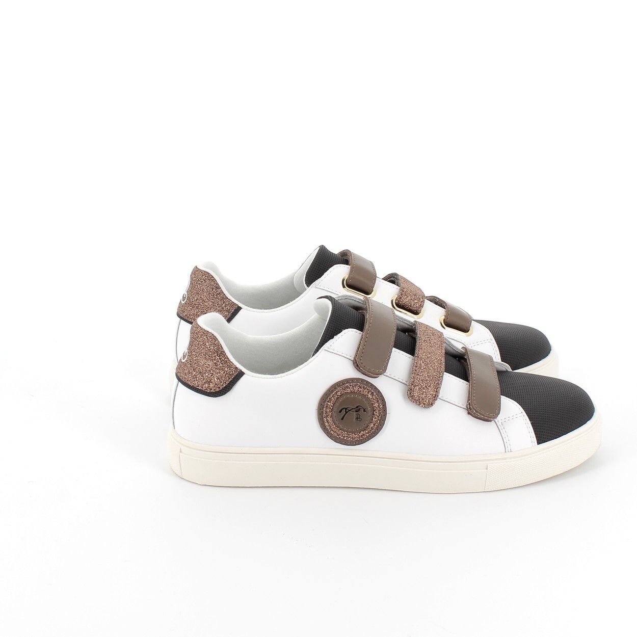 White and black sneakers with a textured brown strap and a round logo patch, featuring a sleek design and a contrasting rubber sole.