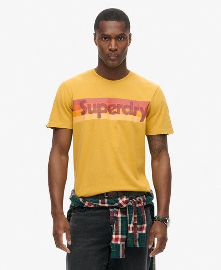 Yellow striped T-shirt featuring a bold retro "Superdry" logo in red and orange, made from soft cotton, styled with a plaid shirt tied around the waist.
