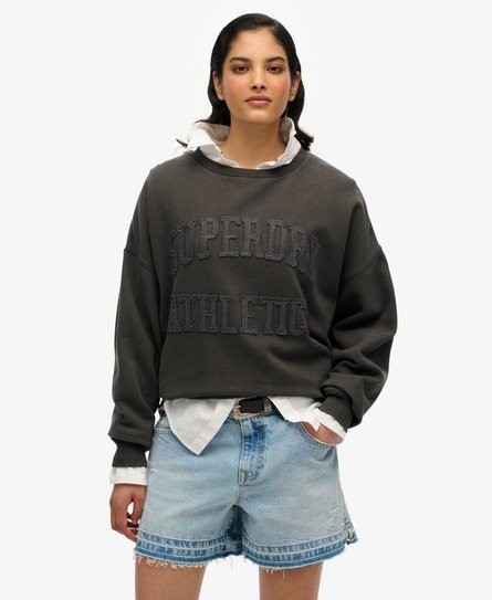Dark grey sweatshirt featuring "Superdry Athletic" tonal applique, relaxed fit, and a crew neck, paired with a white collared shirt and denim shorts.