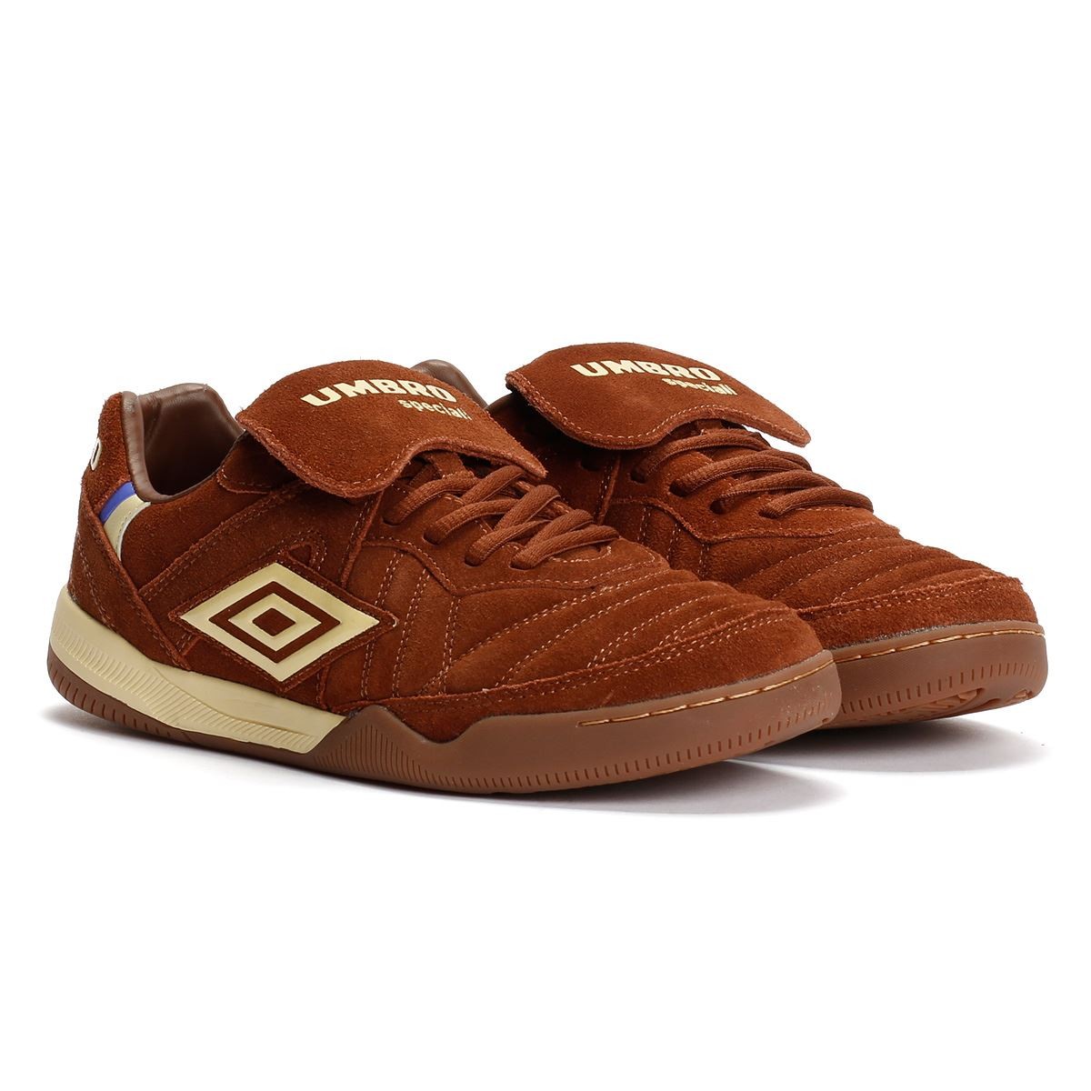 Dark brown suede trainers with cream accents, featuring a Velcro strap, textured upper, and signature Umbro logo on the side.