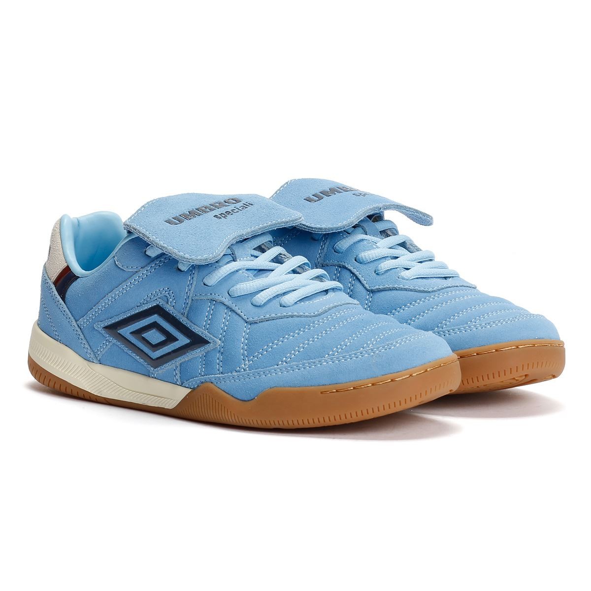 Light blue suede trainers with dark navy accents, featuring a Velcro strap, white sand detailing, and a gum rubber sole, showcasing a classic design by Umbro.