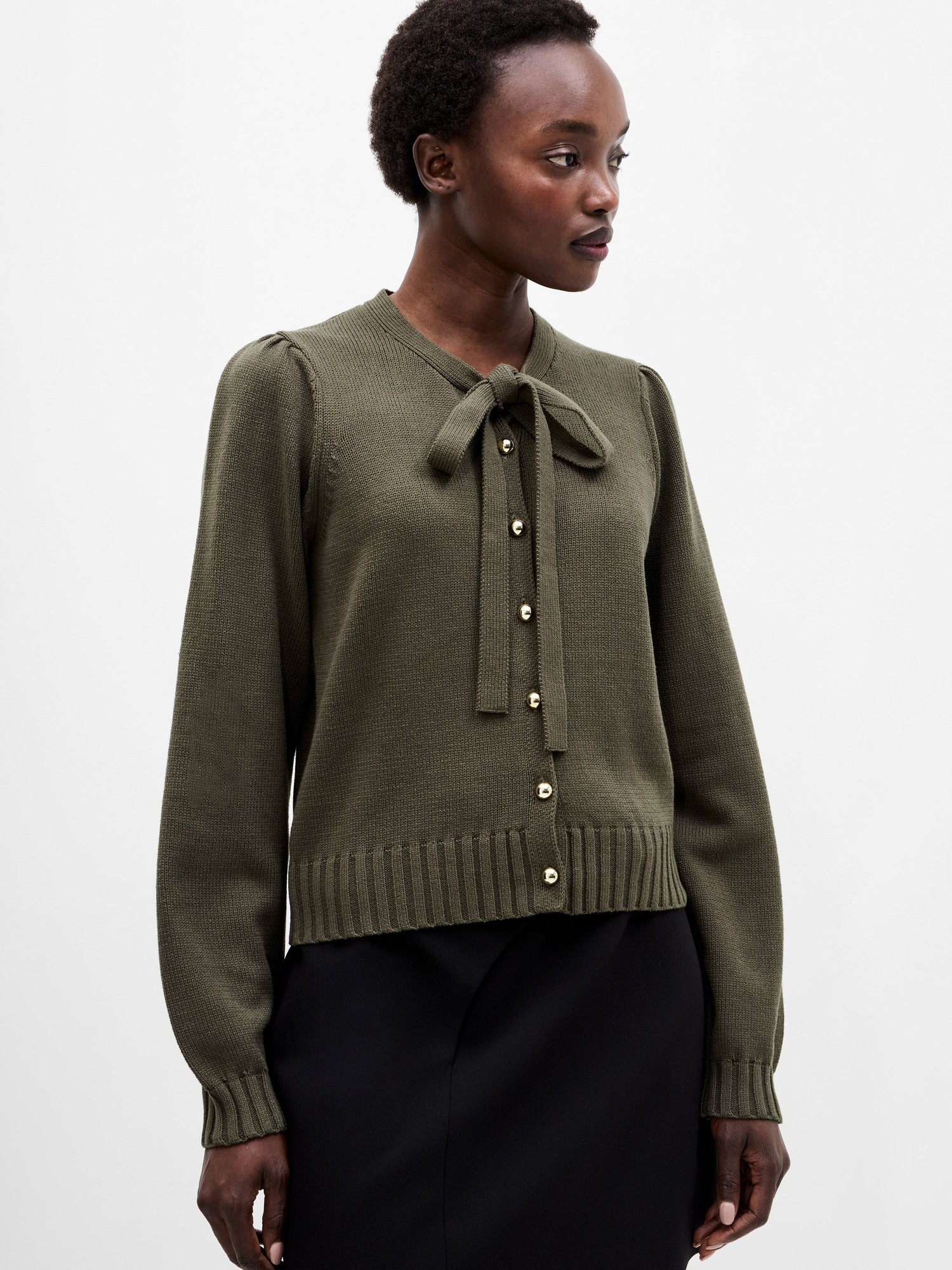 Khaki green long sleeve cardigan featuring a tie neck, ribbed hem, and button closure, made from a textured knit material, styled with a model against a neutral background.