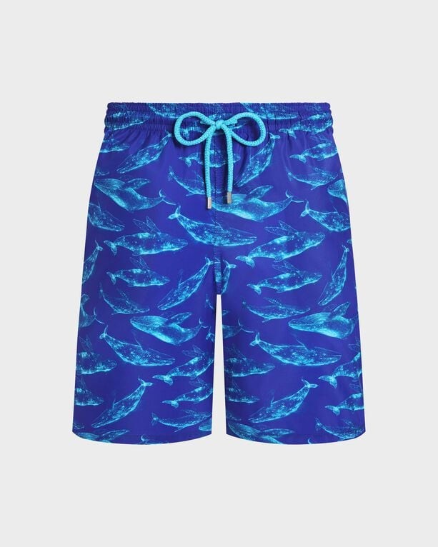 Blue swim shorts featuring a vibrant whale print, made from lightweight, packable material, with an elastic waistband and contrasting turquoise drawstring, ideal for beachwear.