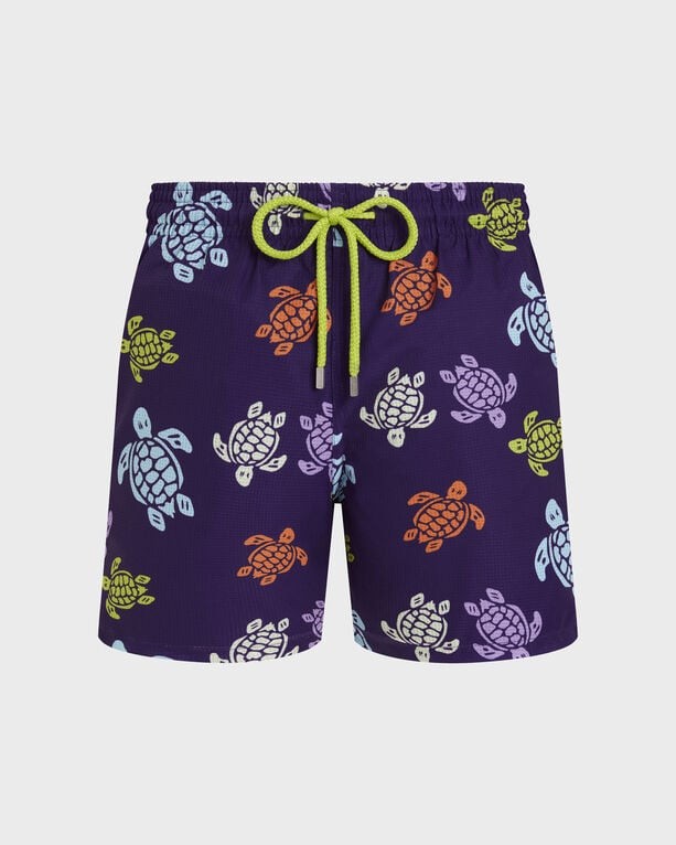 Purple micro-perforated swim shorts featuring a colorful turtle pattern, elastic waistband with a green drawstring, and ultra-light, packable material.