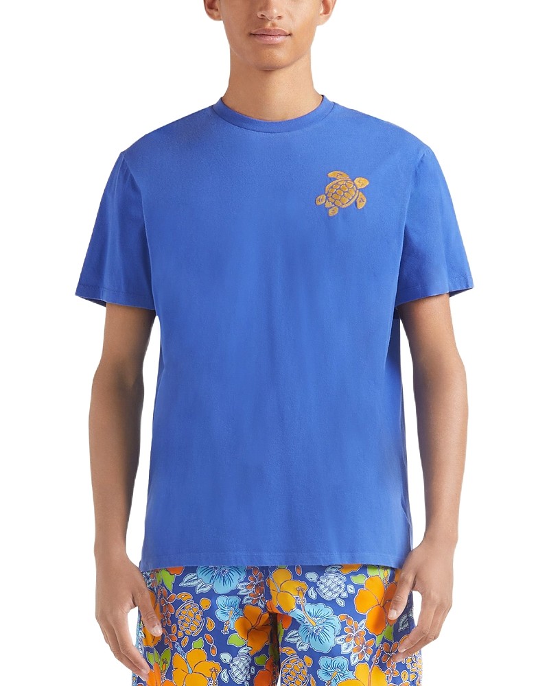 Blue organic cotton T-shirt featuring an embroidered turtle design on the chest, paired with vibrant floral-patterned shorts, model wearing size M.