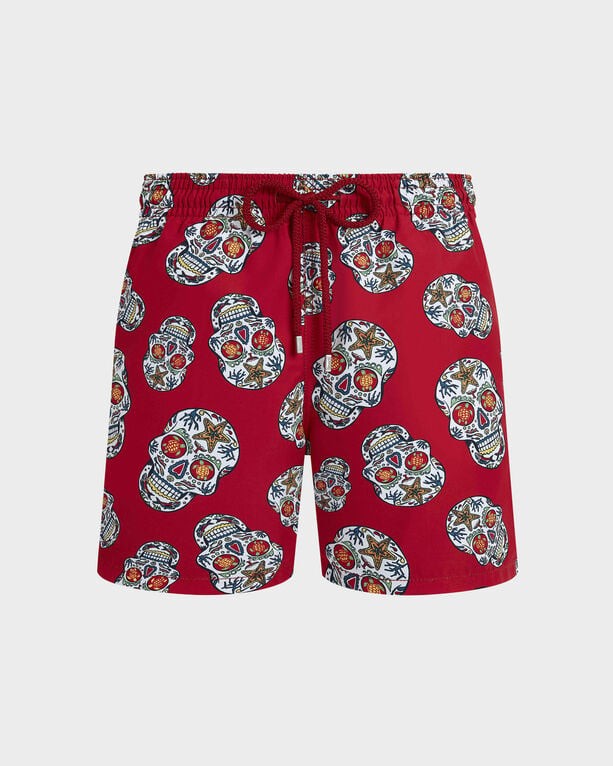 Red swim trunks featuring a Día De Muertos skull pattern, with vibrant colors and a drawstring waist, made from lightweight material, size L.