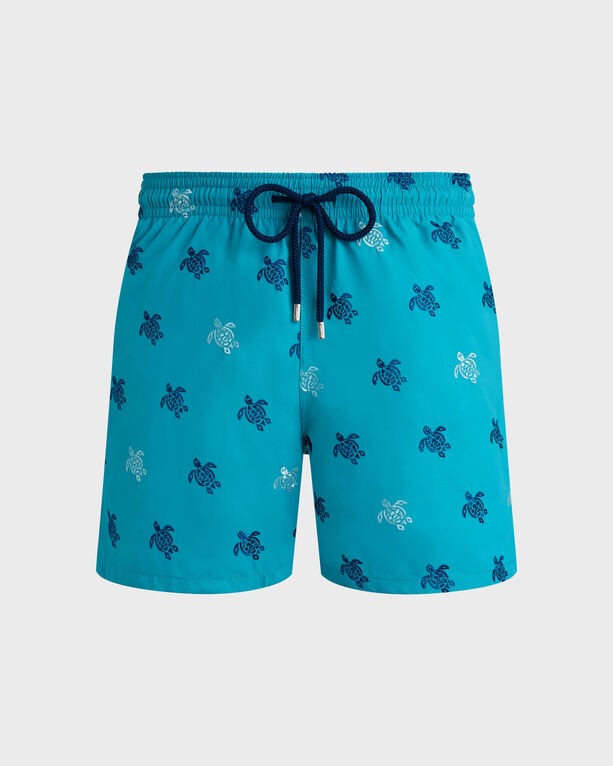 Turquoise swim shorts featuring embroidered turtle designs in blue and white, with an elastic waistband and drawstring, part of a limited edition collection.