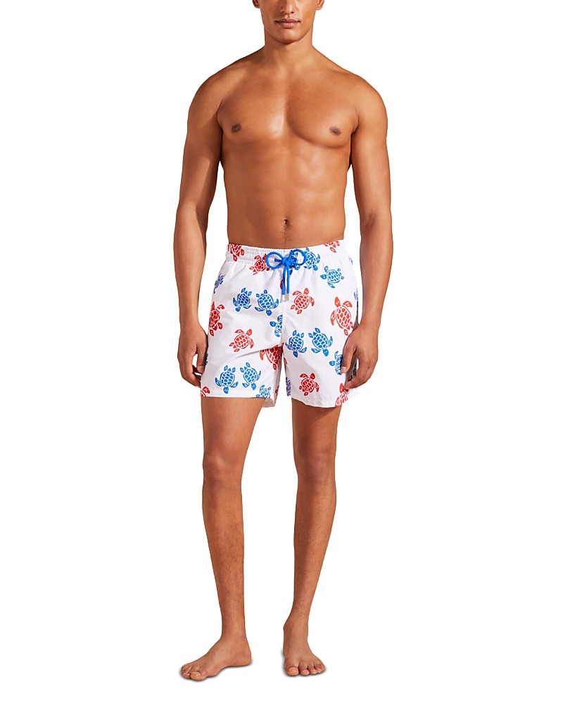 White swim trunks featuring a vibrant red and blue coral print, made from quick-drying material, with an elastic waistband and adjustable drawstring.