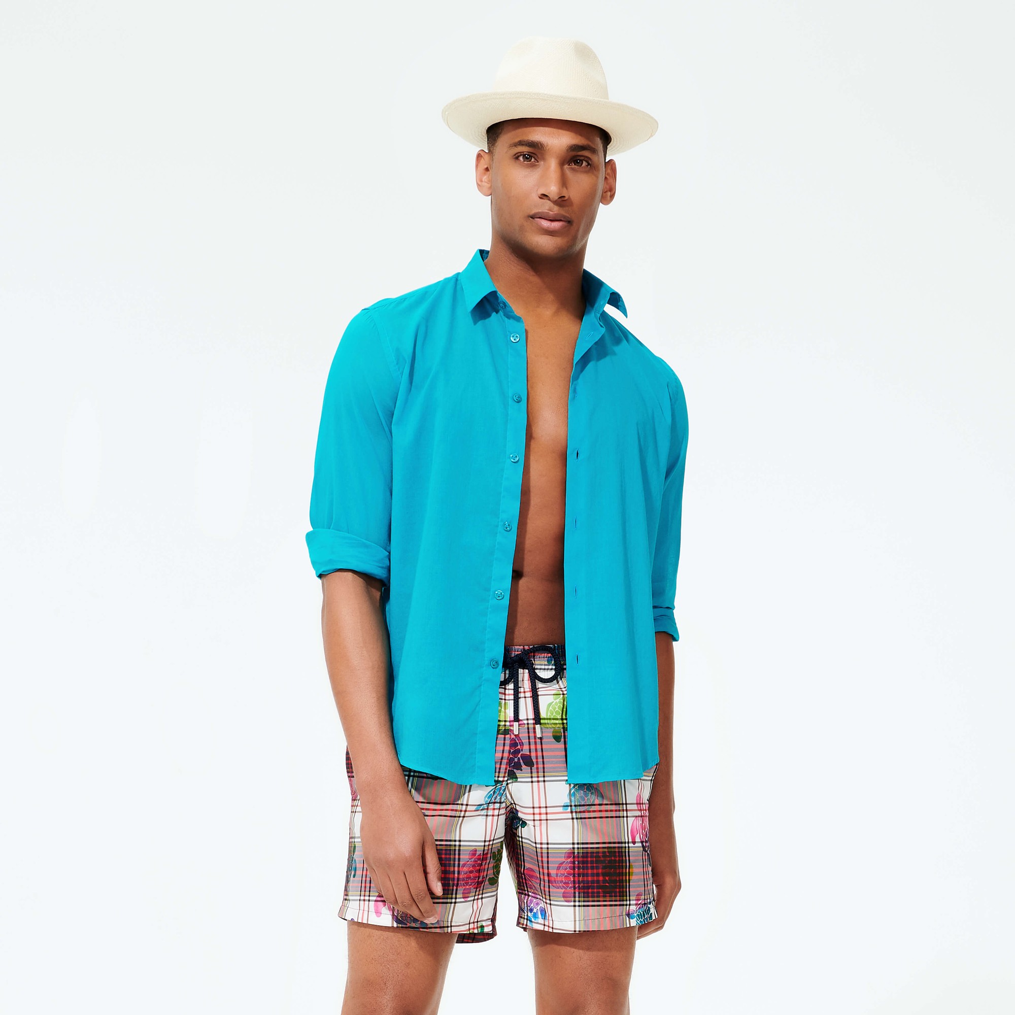 Beige natural straw Panama hat by Vilebrequin, featuring a wide brim, worn by a model in a turquoise shirt and plaid swim shorts.