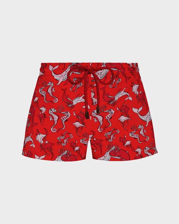 Red swim shorts featuring a playful whale pattern, drawstring waist, and shorty cut, made from lightweight fabric, ideal for beachwear.