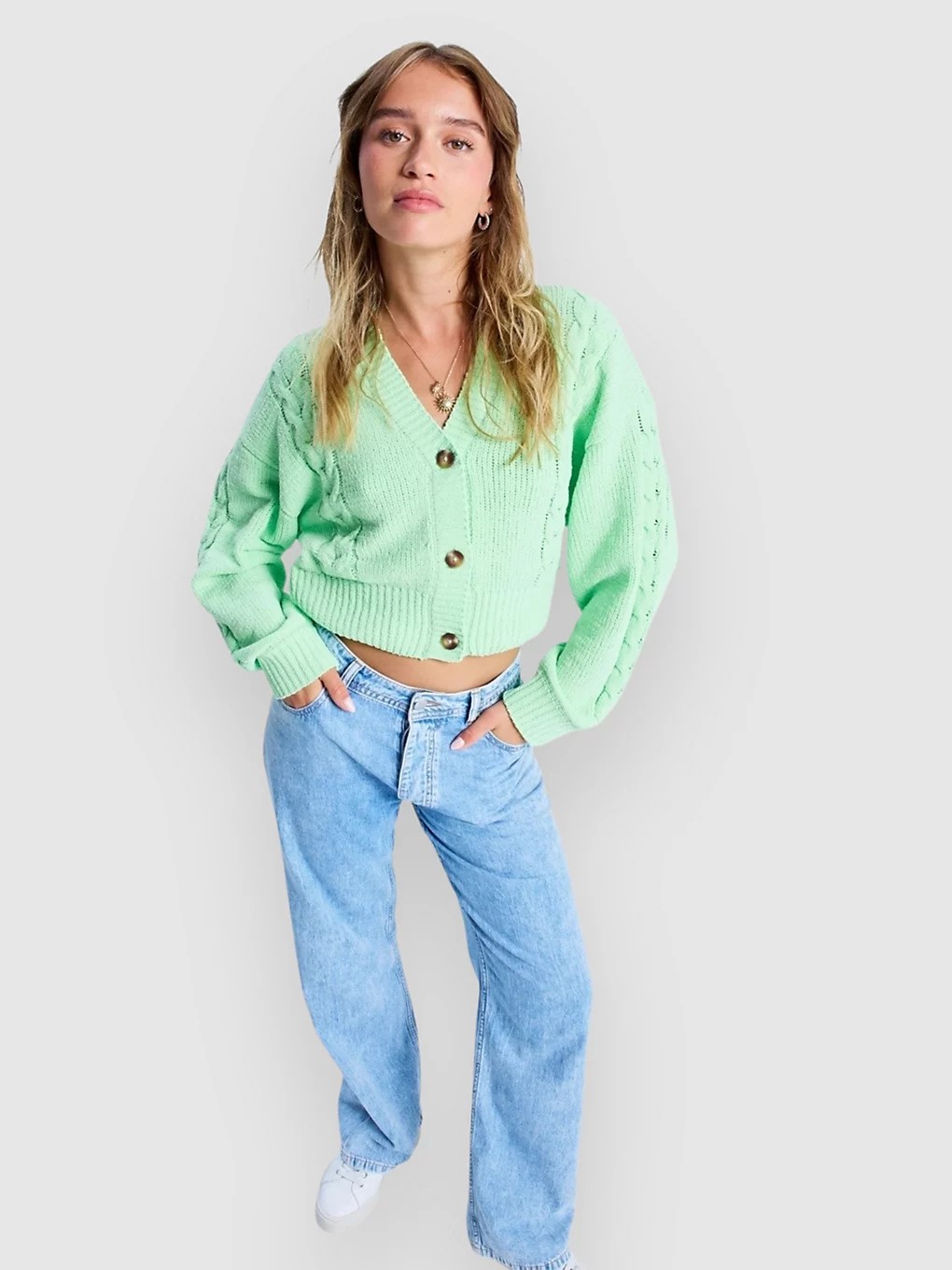 Light green knitted cardigan with a V-neck, button closure, and textured detailing, paired with light blue wide-leg jeans.
