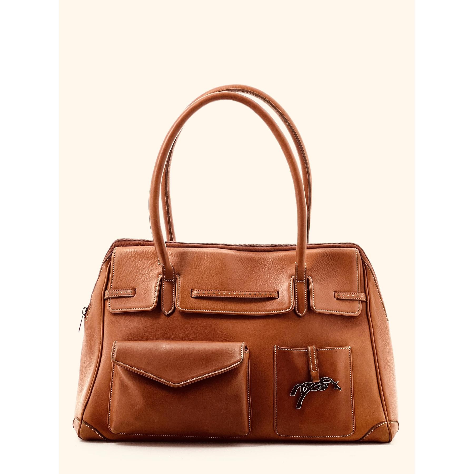 Brown leather handbag with dual handles, featuring a front pocket and subtle stitching details, designed by Pénélope Maëlys.