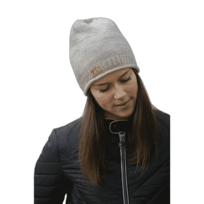Light gray knitted women's beanie hat with a ribbed texture and a small leather logo patch, worn by a woman with long brown hair, dressed in a black jacket.