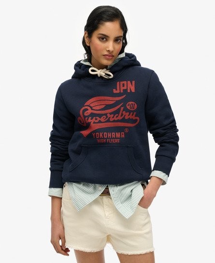 Navy blue women's hooded sweatshirt with a red Superdry logo, featuring a front pocket and a drawstring hood, layered over a light blue and white striped shirt.