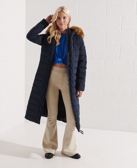 Navy long jacket by Superdry, featuring a quilted design, fur-trimmed hood, and side slits, paired with a blue top and beige flared pants.