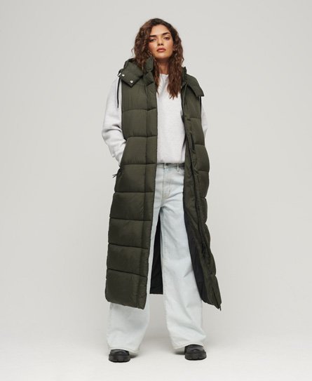 Long sleeveless hooded down jacket in olive green, featuring a quilted design, front zip, and side pockets, worn over a light gray sweatshirt and loose-fitting jeans.