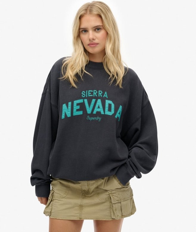 Loose-fitting black sweatshirt with "SIERRA NEVADA" and "Superdry" printed in teal, paired with khaki cargo shorts, worn by a model with long blonde hair.