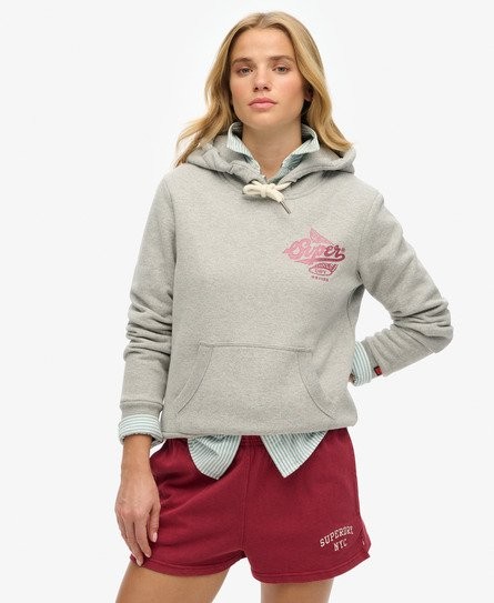 Light grey metallic hooded sweatshirt with a front pocket, featuring a pink Superdry logo, paired with maroon shorts, worn by a model with blonde hair.