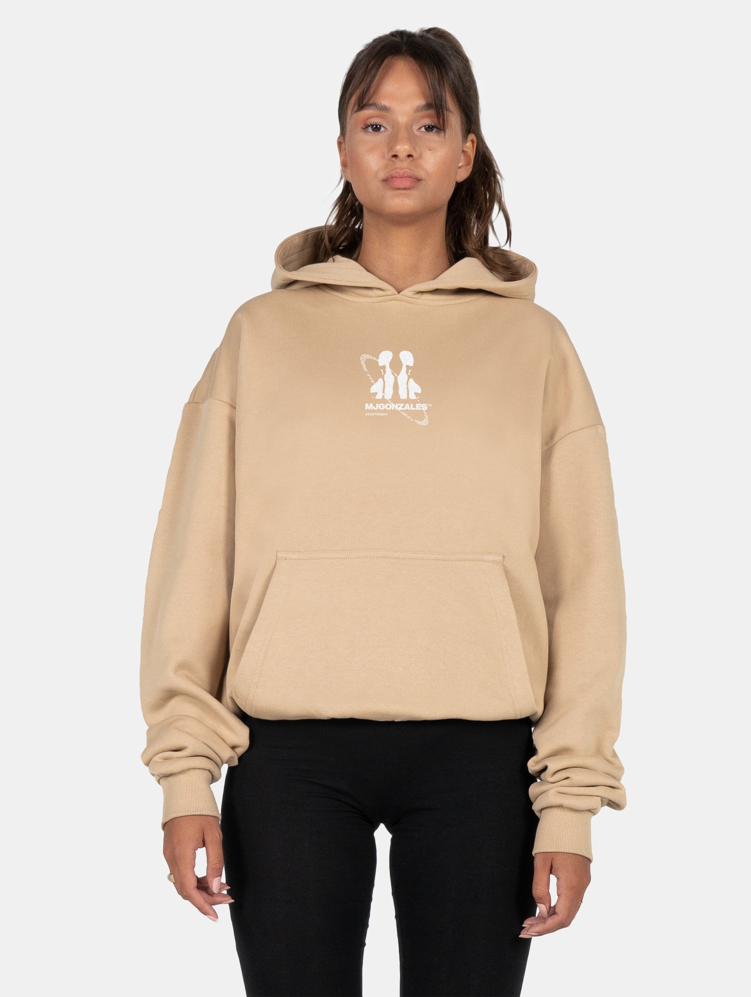 Beige oversized hoodie featuring a front pocket, drawstring hood, and a white MJ Gonzales logo on the chest, paired with black leggings.