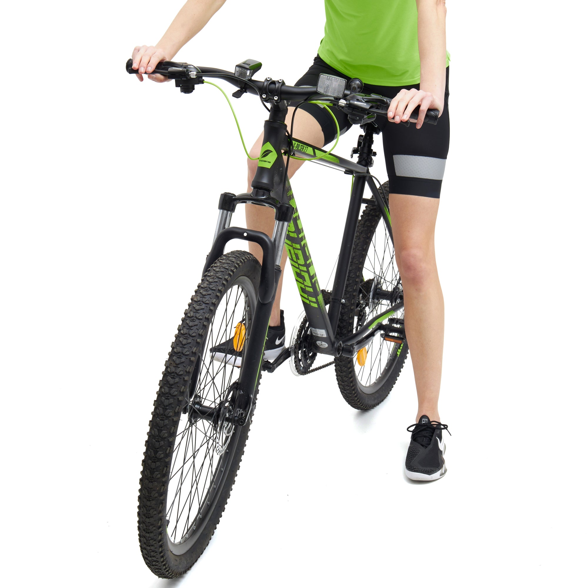 Women's padded cycling shorts in black with reflective grey stripes, paired with a bright green top, worn while riding a black mountain bike.