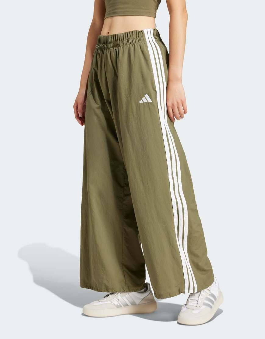 Olive green parachute canvas joggers featuring three white stripes down the sides and an Adidas logo, with a relaxed fit and elastic waistband.