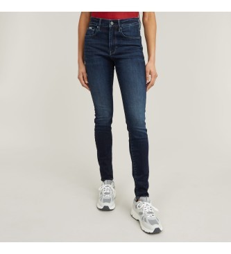 Dark blue women's skinny jeans by G-Star, featuring a high waist, five-pocket design, and a slim fit, paired with a red top and white sneakers.