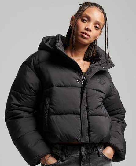 Black puffer jacket with a cropped design, featuring a hood, front zip closure, and signature Superdry logo on the chest, styled with a model showcasing a relaxed fit.