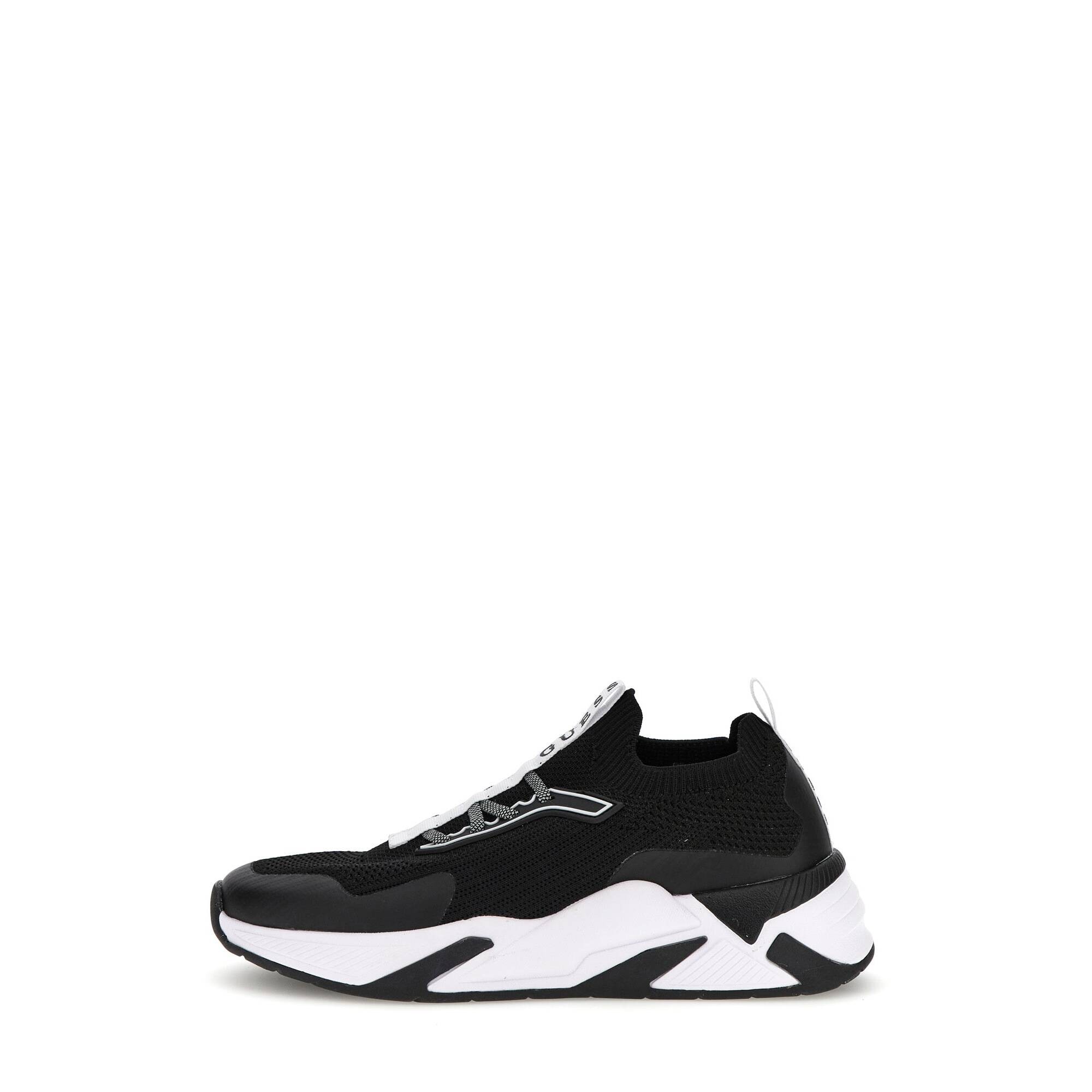 Black and white women's trainers by Guess, featuring a sleek knit upper, elasticized slip-on design, and a chunky sole with distinctive geometric patterns.